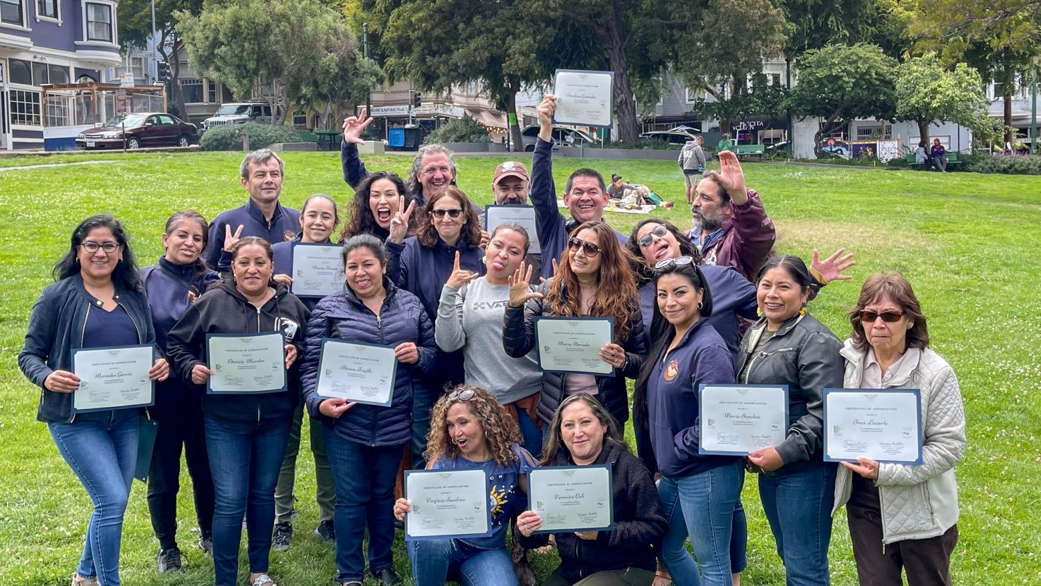 A group of Promotores (community health workers) make funny faces as they gather in a park to take a photo. They are joined with personnel from San Francisco Department of Public Health and UCSF Latinx Center of Excellence