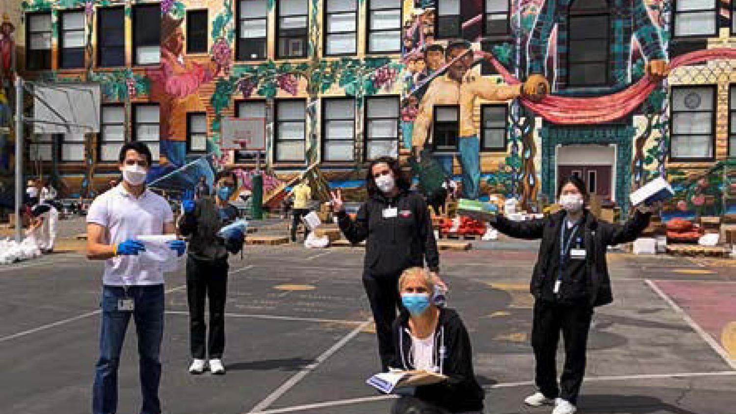 The LCOE team (masked and socially distanced) standing on a school playground  in front of a colorful mural wall.