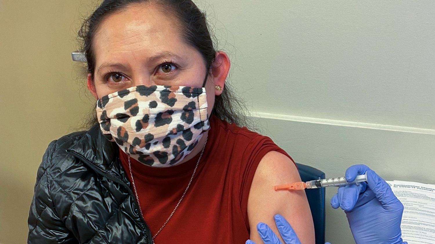 A Latina woman wearing a leopard-print mask, is in a clinic getting her COVID vaccine shot